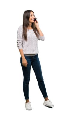 A full-length shot of a Young hispanic brunette woman keeping a conversation with the mobile phone over isolated white background
