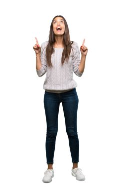 A full-length shot of a Young hispanic brunette woman surprised and pointing up over isolated white background