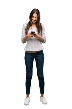 A full-length shot of a Young hispanic brunette woman sending a message with the mobile over isolated white background