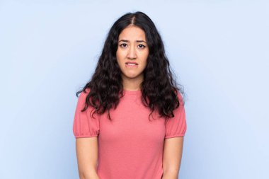 İzole edilmiş mavi arka plan üzerine kazak giyen melez bir kadının şüpheleri ve kafa karıştırıcı bir yüz ifadesi var.