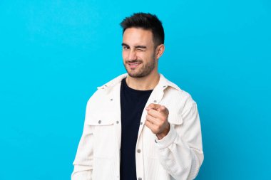Young handsome man over isolated blue background points finger at you