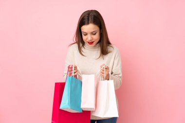 Pembe arka planda izole edilmiş genç bir kız. Elinde alışveriş çantaları var ve içine bakıyor.