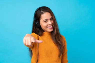 İzole edilmiş mavi duvarda müzik dinleyen genç bir kadın.