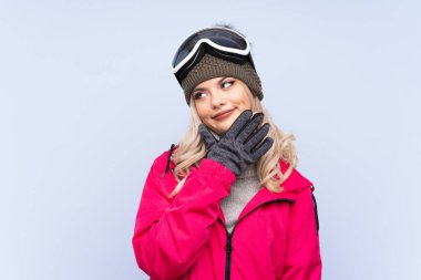 Kar kayağı gözlüklü genç kız izole edilmiş mavi arka planda bir fikir düşünüyor.