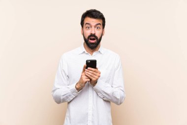 Elinde cep telefonu olan sakallı genç adam şaşırdı ve bir mesaj gönderiyor.