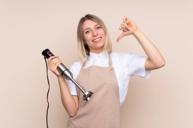 Young blonde woman using hand blender proud and self-satisfied