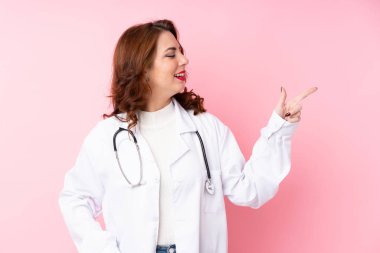 Doktor önlüğü ve işaret eden yüzü olan pembe bir geçmişi olan genç Rus kadın.