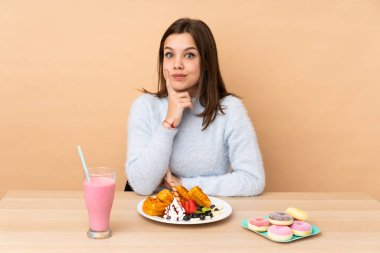 Bej arka planda izole edilmiş waffle yiyen ve ön tarafa bakan genç kız.