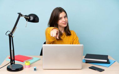 Evinde okuyan öğrenci kız mavi arka planda izole edilmiş. Kendine güvenen bir ifadeyle seni işaret ediyor.