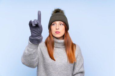 Kışlık şapkalı, mavi arka planda genç kızıl saçlı kadın şeffaf ekrana dokunuyor.