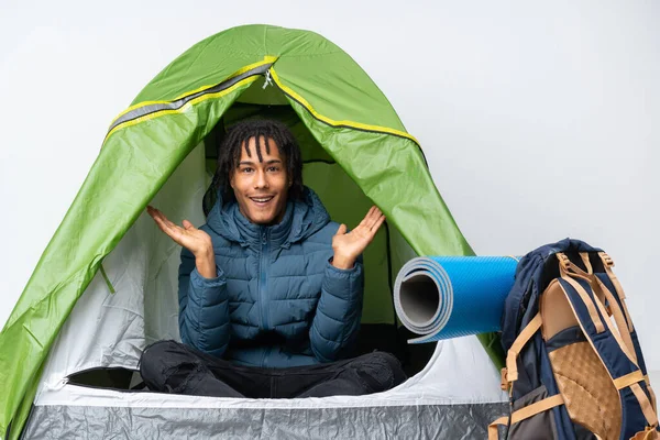 Young african american man inside a camping green tent with shocked facial expression