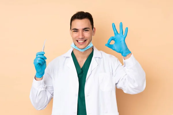 Jovem Dentista Homem Segurando Ferramentas Isoladas Fundo Bege Mostrando Sinal — Fotografia de Stock