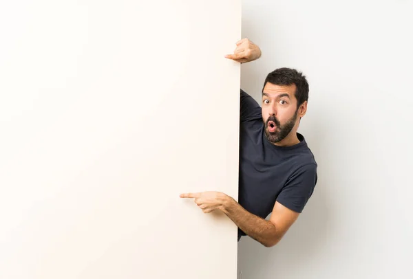 Joven hombre guapo con barba sosteniendo un gran cartel vacío y señalándolo —  Fotos de Stock