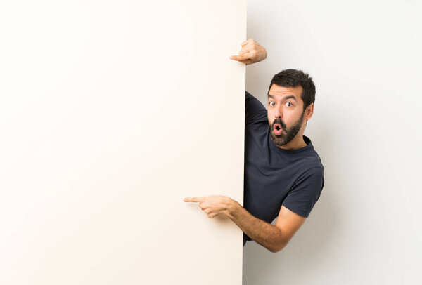 Young handsome man with beard holding a big empty placard and pointing it