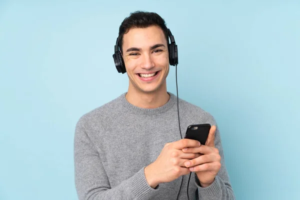 Νεαρός Καυκάσιος Όμορφος Άνδρας Απομονωμένος Μπλε Φόντο Ακούγοντας Μουσική Κινητό — Φωτογραφία Αρχείου