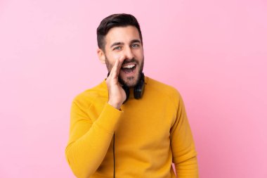 Kulaklıkları olan genç yakışıklı bir adam pembe arka planda ağzı açık bağırıyor.