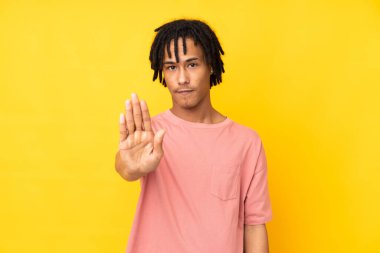 Sarı arka planda izole edilmiş genç Afro-Amerikan bir adam dur hareketi yapıyor.