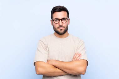 Sakallı, mavi arka planda genç yakışıklı adam kollarını kavuşturuyor.