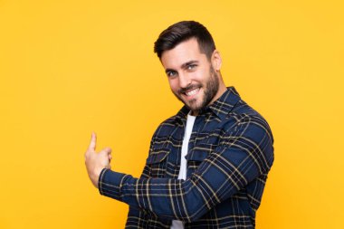 Sakallı yakışıklı genç adam izole edilmiş sarı arka planda geriye bakıyor.