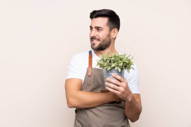 Bahçıvan arka planda bir bitki tutuyor. Yan tarafa bakıyor.