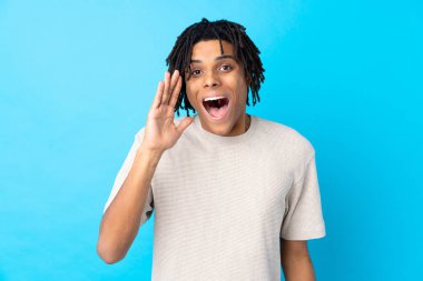 Genç Afro-Amerikalı, mavi arka planda, şaşırmış ve şok olmuş bir yüz ifadesi var.