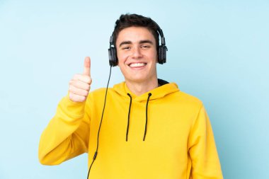Genç beyaz adam mor arka planda izole edilmiş müzik dinliyor ve başparmağını kaldırıyor.