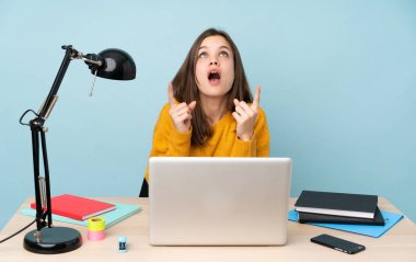 Evinde okuyan öğrenci kız mavi arka planda izole edilmiş, şaşırmış ve işaret ediyor