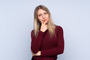 Soyutlanmış mavi arka plan düşünen genç sarışın kadın.