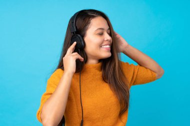 İzole edilmiş mavi duvarda müzik dinleyen genç bir kadın.