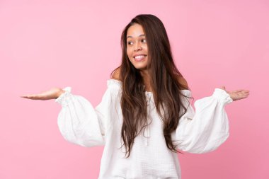 Young Brazilian girl over isolated pink background holding copyspace with two hands