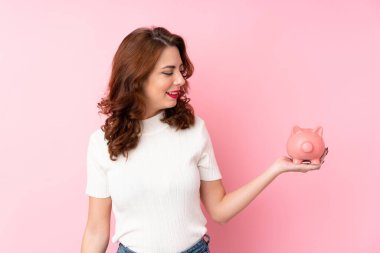 Soyutlanmış pembe arka planı olan genç bir Rus kadın büyük bir kumbara tutuyor.