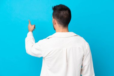 Young handsome man over isolated blue background pointing back with the index finger