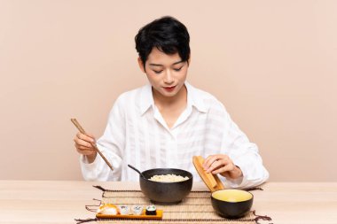 Genç Asyalı kız bir kase erişte ve suşiyle masada.