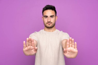Soyutlanmış mor arka planı olan yakışıklı genç adam dur hareketi yapıyor ve hayal kırıklığına uğruyor.