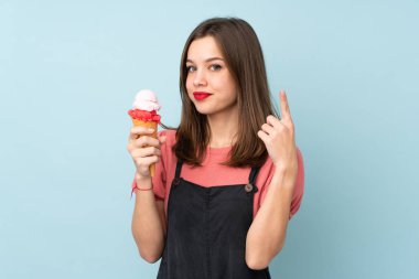 Kornet dondurması tutan genç kız mavi arka planda izole edilmiş. Harika bir fikre işaret ediyor.