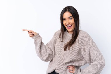 İzole edilmiş beyaz arka planda genç esmer bir kadın parmak işareti yapıyor ve bir ürün sunuyor.
