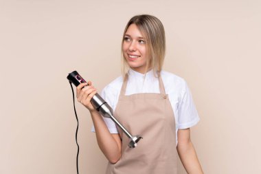 Sarışın bir kadın el blenderi kullanıyor.