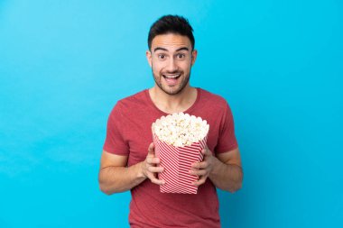 Soyutlanmış mavi arka planda genç yakışıklı bir adam elinde koca bir kova patlamış mısır tutuyor.