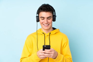 Genç beyaz adam mor arka planda izole edilmiş müzik dinliyor ve cep telefonu arıyor.