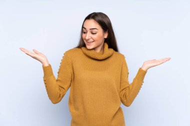 Mavi arka planda izole edilmiş genç beyaz kadın iki eliyle kopyalama alanı tutuyor.