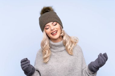Kışlık şapkalı genç kız mavi arka planda gülüyor.