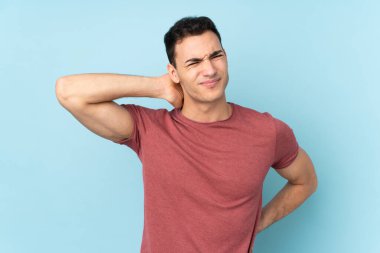 Mavi arka planda boynu ağrıyan, beyaz, yakışıklı genç bir adam.