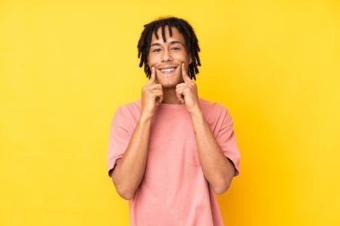 Genç Afrikalı Amerikalı adam sarı arka planda izole edilmiş mutlu ve hoş bir ifadeyle gülümsüyor.