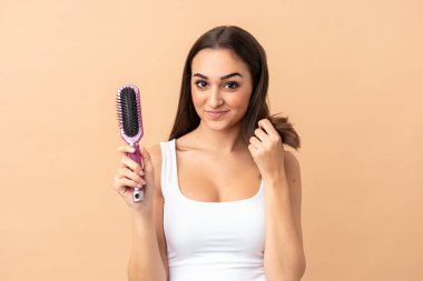 Genç beyaz kadın bej arka planda saç tarağıyla izole edilmiş.