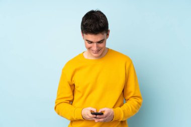 Mor arka planda izole edilmiş beyaz, yakışıklı bir genç cep telefonuyla bir mesaj gönderiyor.