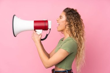 Pembe arka planda izole edilmiş kıvırcık saçlı genç sarışın kadın megafondan bağırıyor.