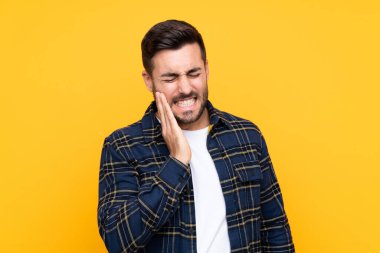 Sakallı, genç, yakışıklı, soyutlanmış, sarı arka planlı, diş ağrısı olan bir adam.