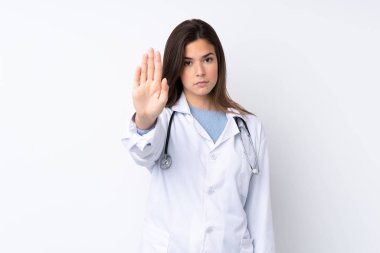 İzole edilmiş beyaz bir geçmişi olan genç bir kız doktor önlüğü giyiyor ve dur işareti yapıyor.