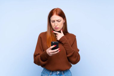 Genç kızıl saçlı kadın mavi arka plan üzerinde düşünüp mesaj gönderiyor.