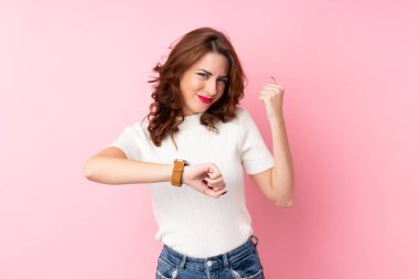 Kol saati ve şanslı yüz ifadesiyle izole edilmiş pembe arka planı olan genç bir Rus kadın.